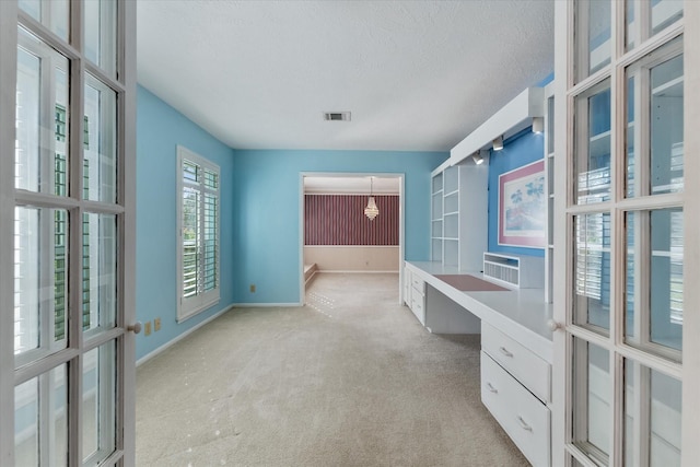 office area with built in desk, light colored carpet, and a textured ceiling