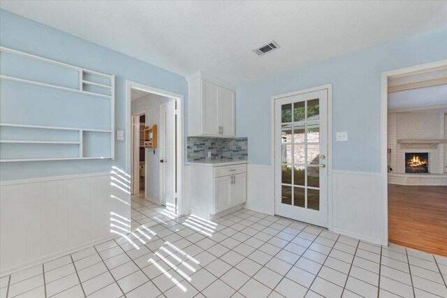 kitchen featuring white cabinetry, light tile patterned floors, decorative backsplash, and a fireplace