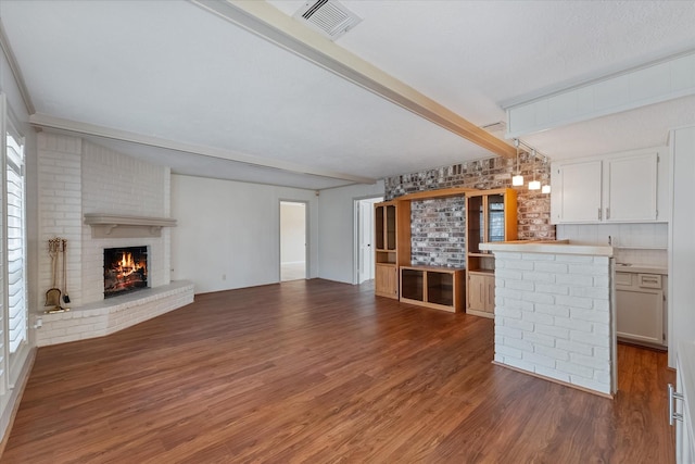 unfurnished living room featuring dark wood-type flooring, a fireplace, beam ceiling, and a textured ceiling