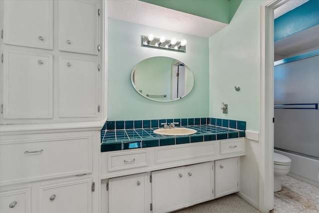 full bathroom with shower / bath combination with glass door, tile patterned flooring, vanity, toilet, and a textured ceiling