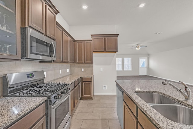 kitchen with stainless steel appliances, light stone counters, ceiling fan, and sink