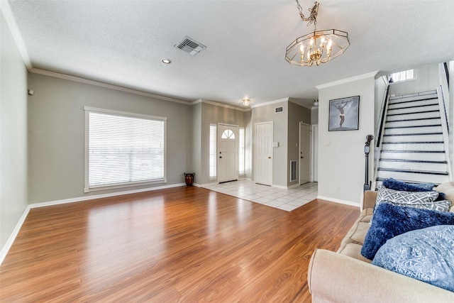 foyer entrance with a textured ceiling, a notable chandelier, light wood-type flooring, and ornamental molding