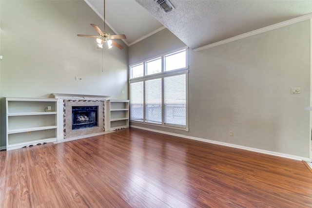 unfurnished living room with a textured ceiling, ceiling fan, crown molding, wood-type flooring, and a tiled fireplace