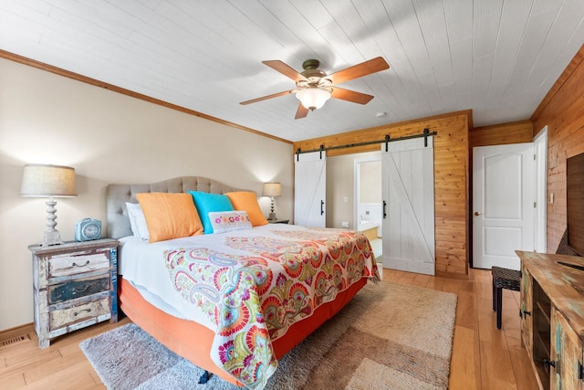 bedroom featuring ceiling fan, a barn door, wood walls, wood ceiling, and light wood-type flooring