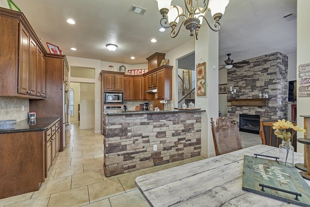 kitchen with ceiling fan with notable chandelier, a fireplace, appliances with stainless steel finishes, decorative light fixtures, and kitchen peninsula