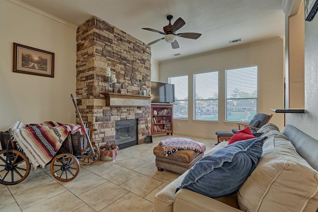 tiled living room with ceiling fan, a stone fireplace, and crown molding