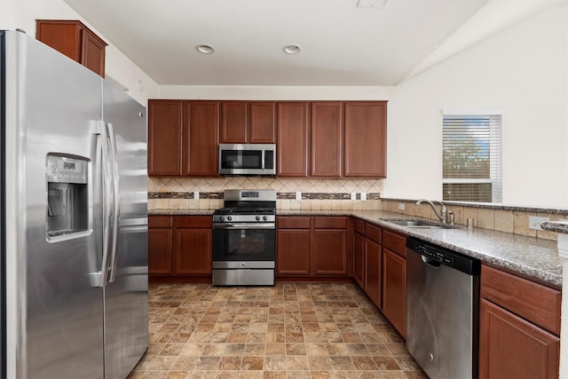 kitchen with sink, vaulted ceiling, decorative backsplash, dark stone countertops, and appliances with stainless steel finishes