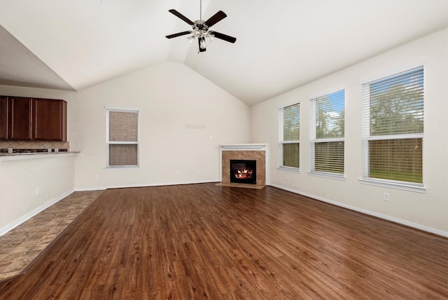 unfurnished living room featuring dark hardwood / wood-style floors, ceiling fan, lofted ceiling, and a tiled fireplace