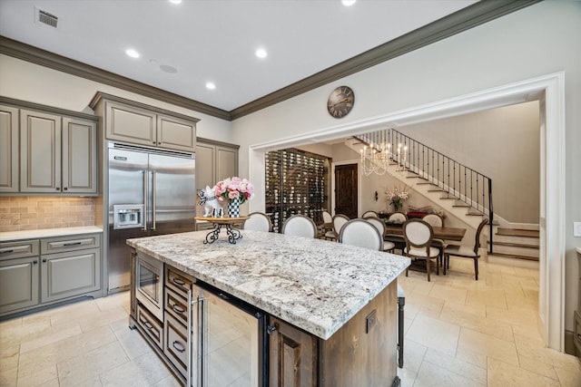 kitchen with light stone countertops, a kitchen breakfast bar, built in appliances, a center island, and wine cooler