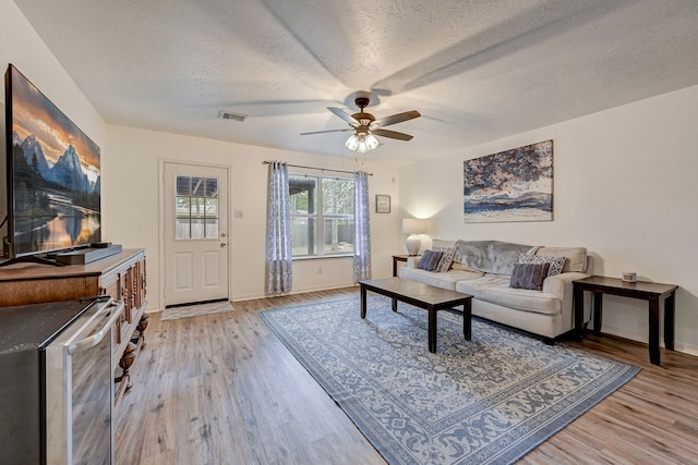 living room with a textured ceiling, light hardwood / wood-style floors, and ceiling fan