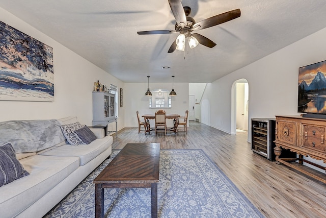 living room with ceiling fan, beverage cooler, a textured ceiling, and wood-type flooring