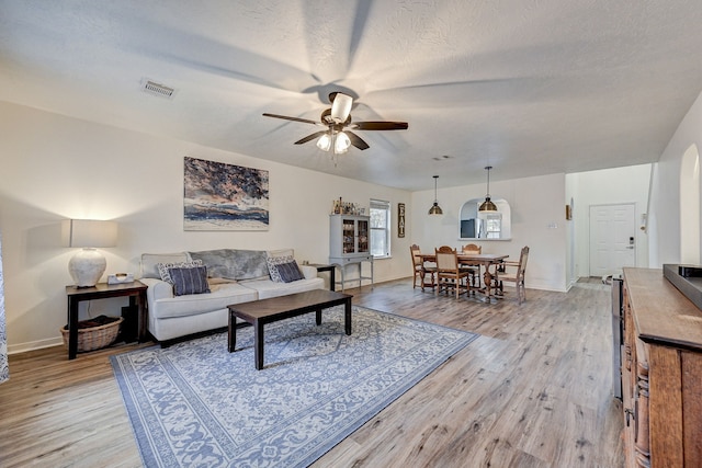 living room featuring a textured ceiling, light hardwood / wood-style flooring, and ceiling fan