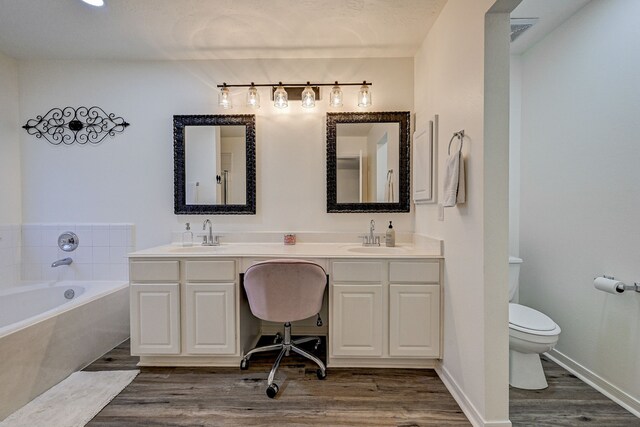 bathroom with hardwood / wood-style flooring, a relaxing tiled tub, toilet, and vanity