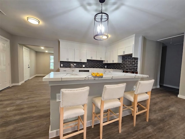 kitchen with white cabinets, a breakfast bar, pendant lighting, and light stone countertops