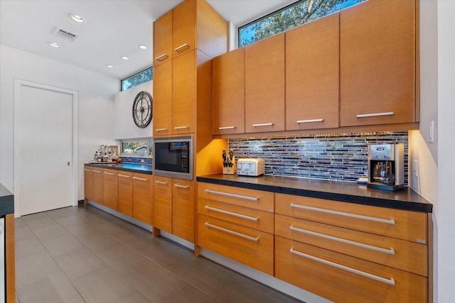 kitchen featuring dark countertops, visible vents, black microwave, and tasteful backsplash