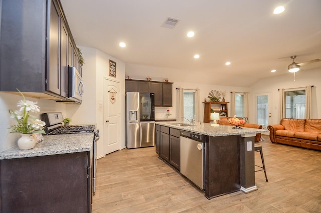 kitchen featuring appliances with stainless steel finishes, light stone counters, sink, a center island with sink, and light hardwood / wood-style flooring