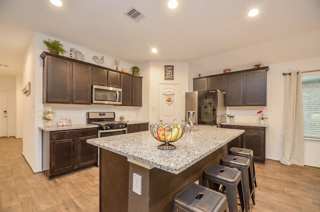 kitchen with dark brown cabinetry, a kitchen island with sink, stainless steel appliances, and light stone counters