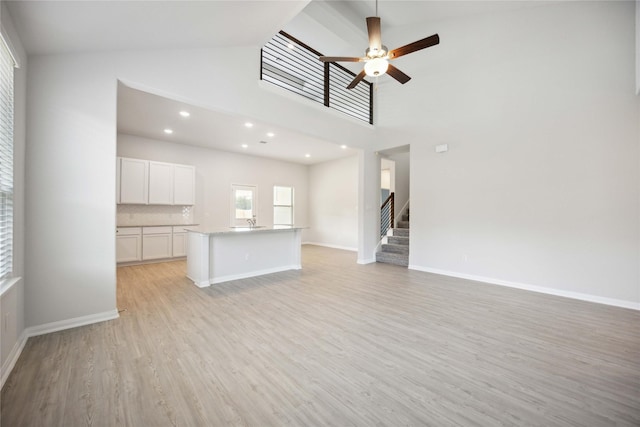 unfurnished living room featuring a towering ceiling, light wood-type flooring, and ceiling fan