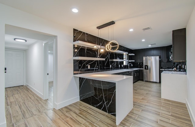 kitchen featuring kitchen peninsula, stainless steel refrigerator with ice dispenser, hanging light fixtures, and sink