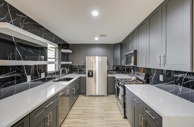 kitchen featuring light stone countertops, appliances with stainless steel finishes, gray cabinets, and sink