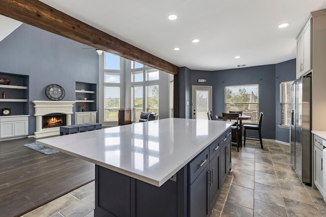 kitchen featuring stainless steel refrigerator with ice dispenser, built in features, beamed ceiling, white cabinets, and a center island