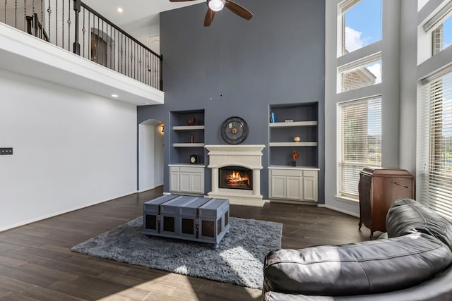 living room with built in shelves, dark hardwood / wood-style flooring, ceiling fan, and a high ceiling