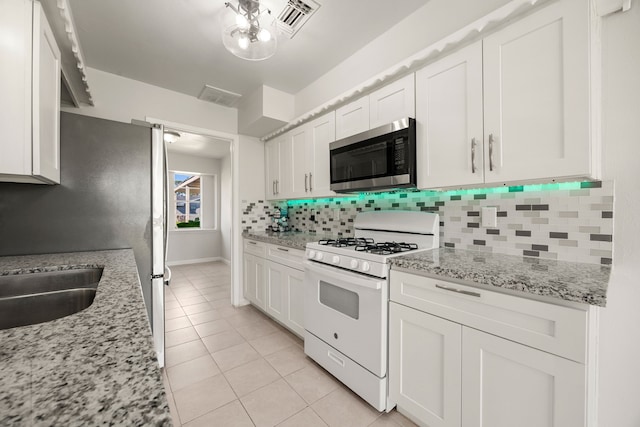 kitchen with white cabinets, light tile patterned floors, stainless steel appliances, and light stone counters