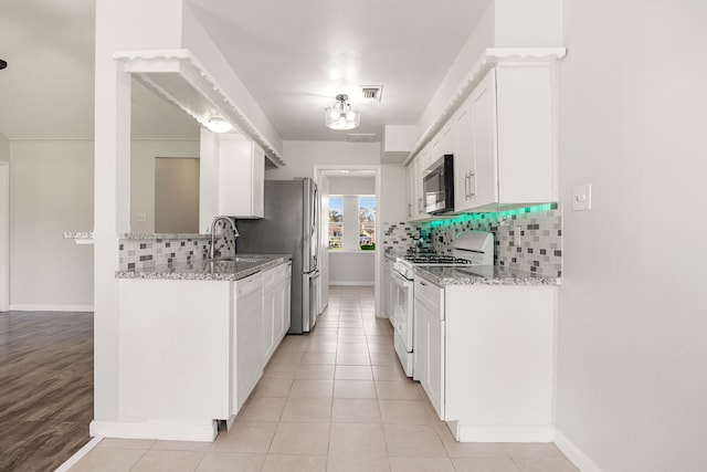 kitchen featuring stove, tasteful backsplash, light stone counters, sink, and white cabinetry