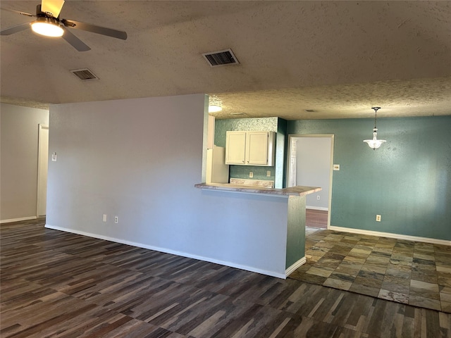 kitchen with kitchen peninsula, dark hardwood / wood-style flooring, a textured ceiling, decorative light fixtures, and white cabinets