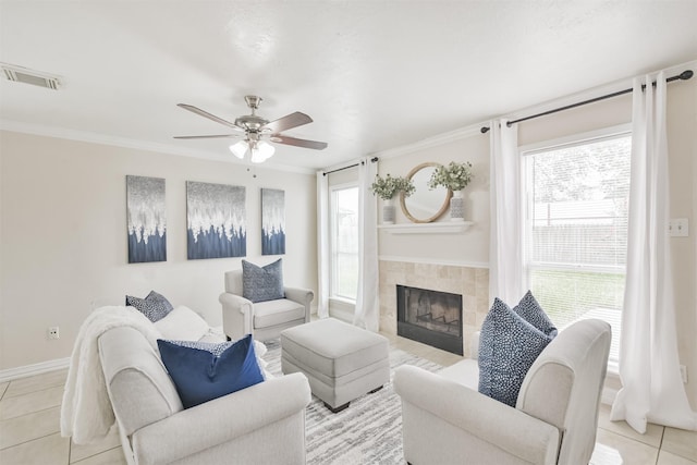 living room featuring a tile fireplace, light tile patterned floors, ceiling fan, and crown molding