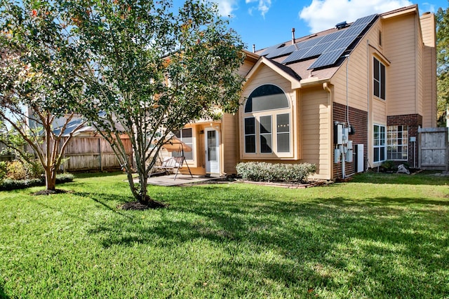 view of front of home featuring brick siding, a patio, a front yard, roof mounted solar panels, and a fenced backyard