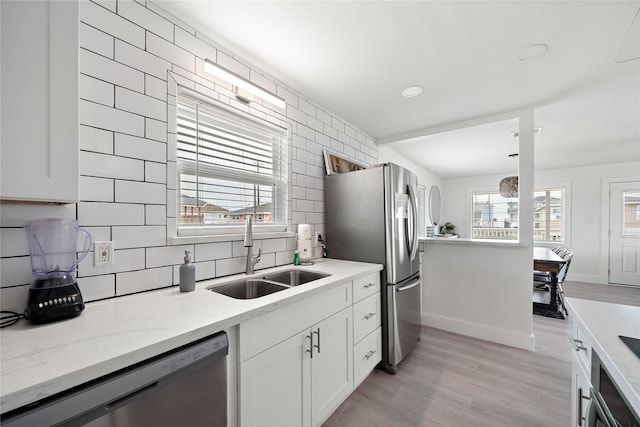 kitchen featuring light stone countertops, backsplash, stainless steel appliances, sink, and white cabinets