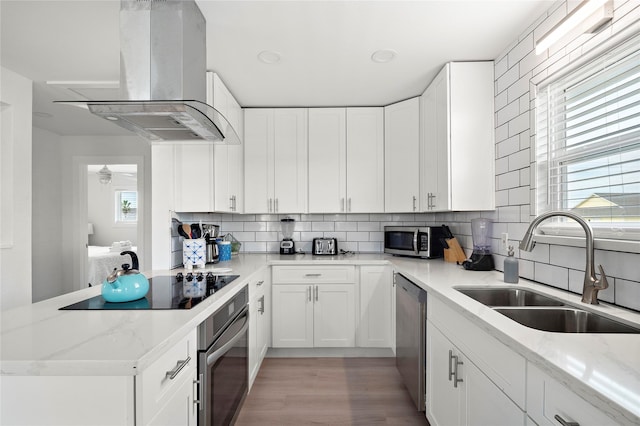 kitchen featuring backsplash, white cabinets, wall chimney range hood, sink, and appliances with stainless steel finishes