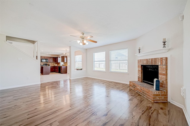 unfurnished living room featuring ceiling fan with notable chandelier, light hardwood / wood-style floors, and a brick fireplace