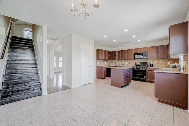 kitchen featuring a center island, hanging light fixtures, tasteful backsplash, light stone counters, and black appliances