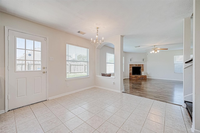 unfurnished living room with a fireplace, light tile patterned flooring, and ceiling fan with notable chandelier