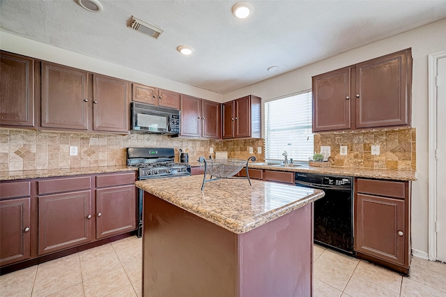 kitchen with a center island, black appliances, sink, light stone countertops, and light tile patterned floors