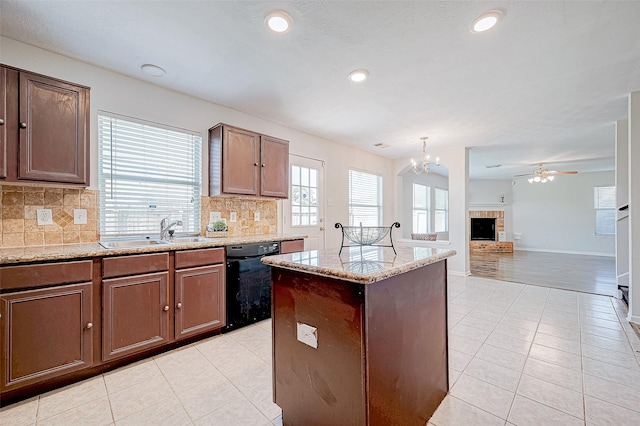 kitchen featuring ceiling fan with notable chandelier, sink, a brick fireplace, black dishwasher, and a kitchen island