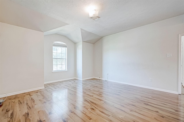 spare room with lofted ceiling, a textured ceiling, and light hardwood / wood-style flooring