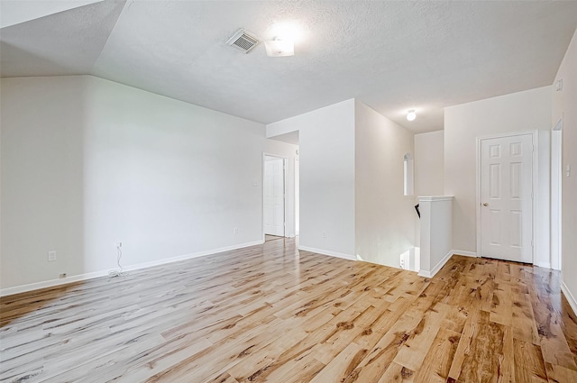 empty room featuring vaulted ceiling, light hardwood / wood-style floors, and a textured ceiling