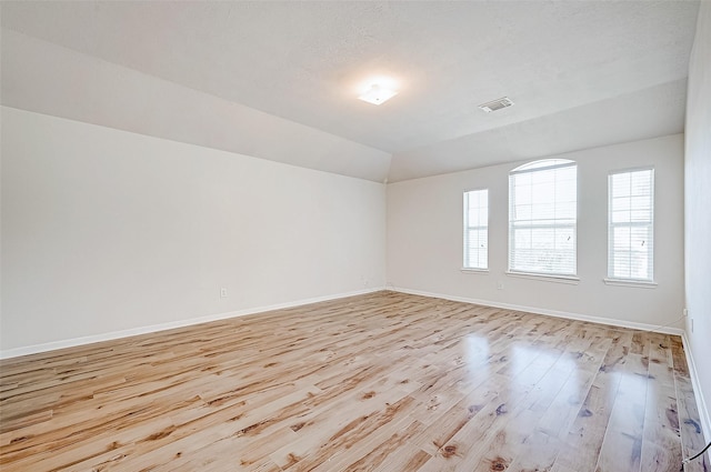 unfurnished room with a textured ceiling, light hardwood / wood-style flooring, and vaulted ceiling