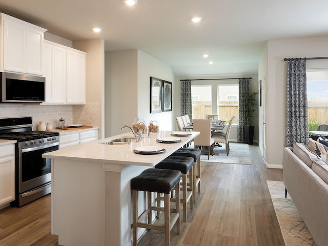 kitchen with white cabinetry, a kitchen island with sink, light hardwood / wood-style floors, and appliances with stainless steel finishes