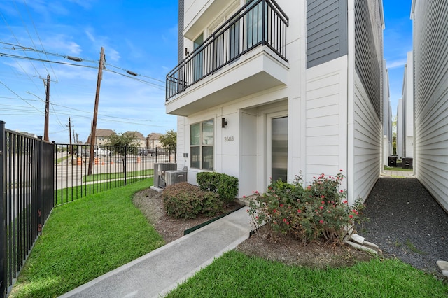 doorway to property featuring a balcony, central AC unit, and a lawn