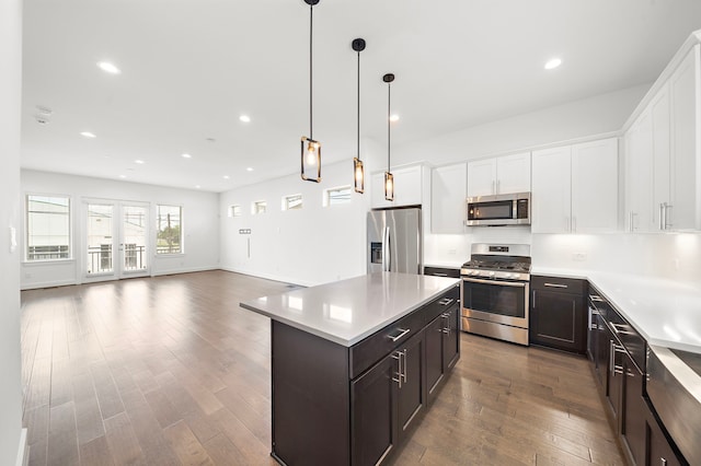 kitchen with white cabinetry, stainless steel appliances, decorative light fixtures, a kitchen island, and hardwood / wood-style flooring