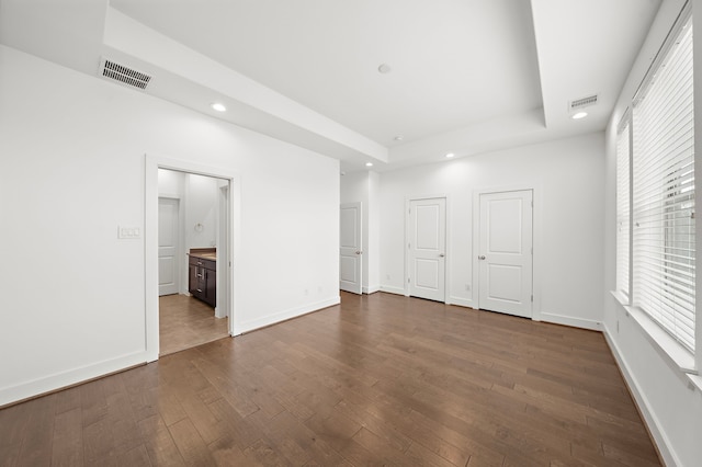 unfurnished bedroom featuring a raised ceiling, two closets, dark hardwood / wood-style flooring, and ensuite bath