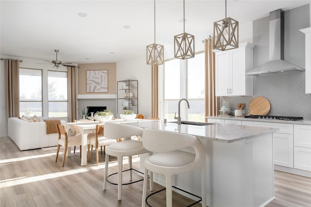 kitchen featuring backsplash, sink, wall chimney range hood, pendant lighting, and white cabinetry