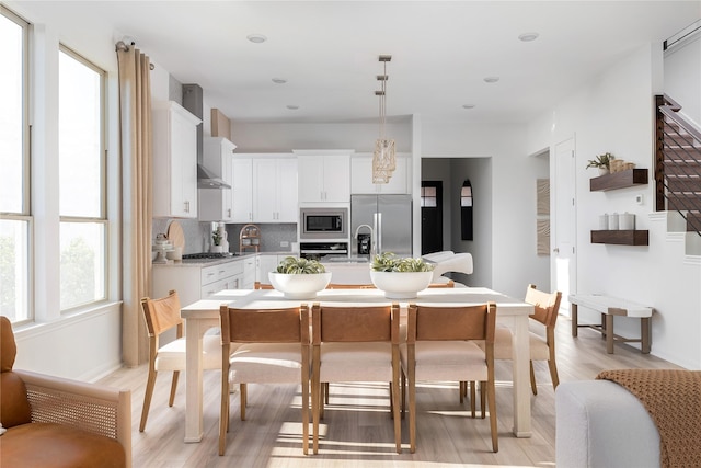 kitchen with hanging light fixtures, wall chimney range hood, a kitchen island with sink, white cabinets, and appliances with stainless steel finishes