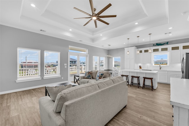 living room featuring ceiling fan with notable chandelier, a raised ceiling, light wood-type flooring, and sink