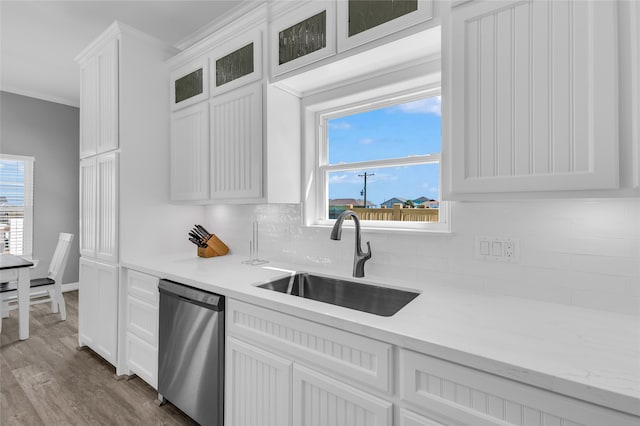 kitchen with a wealth of natural light, dishwasher, sink, white cabinets, and ornamental molding