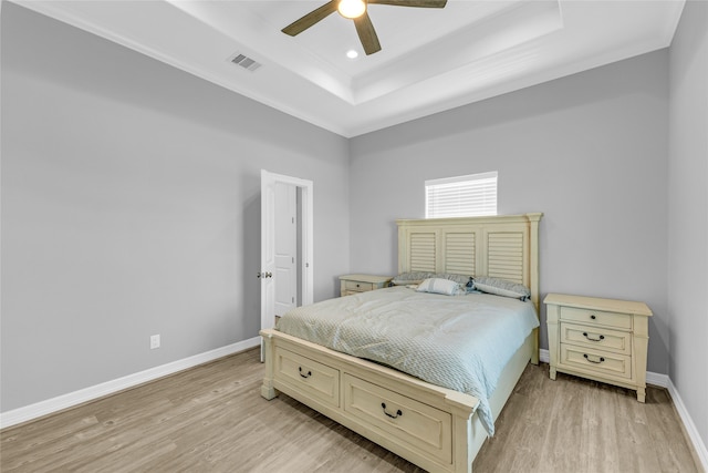 bedroom with ceiling fan, a raised ceiling, crown molding, and light hardwood / wood-style flooring